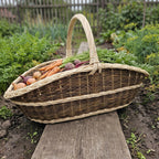 Extra large garden trug basket with a twisted handle, handwoven from willow and filled with carrots and beetroot on a plank between vegetable beds.