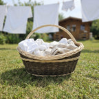 Wicker harvest carrier filled with white laundry on a sunny lawn, with linen drying on a washing line in front of a garden house.
