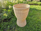 Willow pedestal display basket with an hourglass shape, flared top and wide foot, standing on the grass in a garden