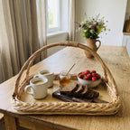 Handwoven willow wicker tray with handles and a wooden base, set with coffee mugs, honey, strawberries and rye bread on a farmhouse kitchen table