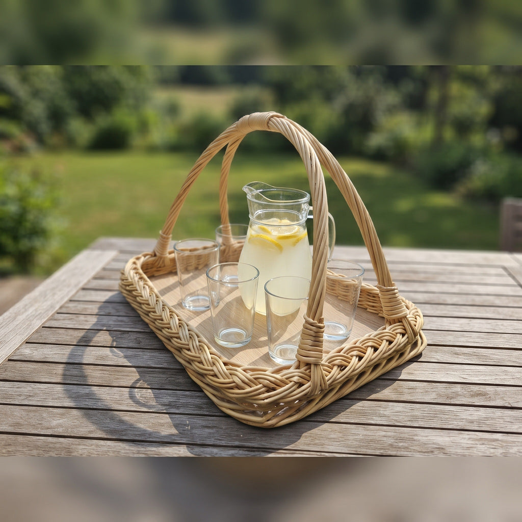 Handwoven willow serving tray with handles carrying a glass jug of lemonade and drinking glasses on a wooden garden table