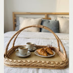 Wicker breakfast in bed tray woven from willow, with cups of coffee, croissants and a jar of jam on a bed with linen pillows
