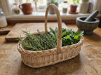 Willow herb basket trug with handle filled with fresh rosemary, thyme and sage on a kitchen table with a mortar and pestle