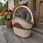Decorative wicker basket with handle holding dried lavender and wildflowers on a wooden porch beside potted geraniums