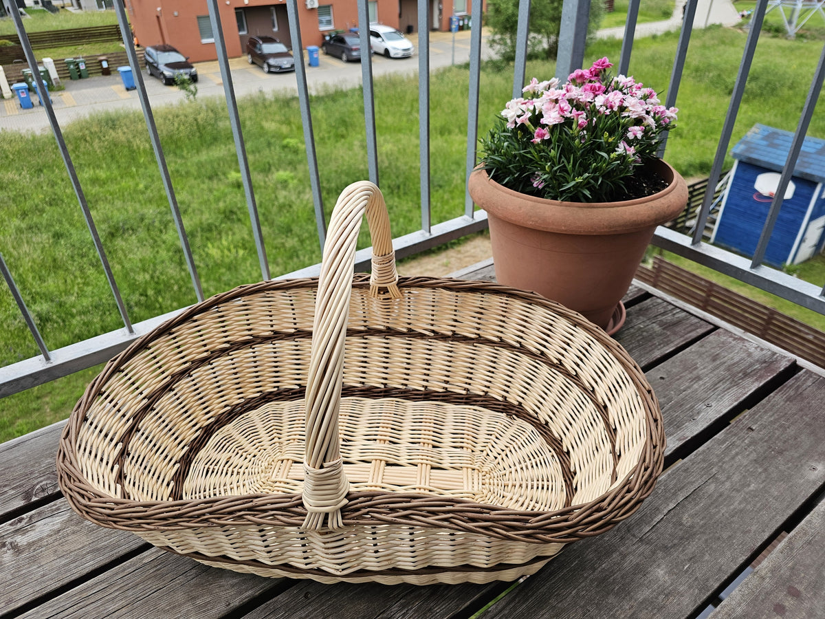 Side view of the extra large handwoven willow trug with a twisted handle, showing its low boat-shaped body on a table