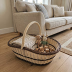 Extra large willow trug with handle used as a toy and blanket basket beside a sofa, with teddy bears and wooden blocks