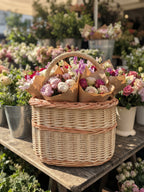 Wicker basket with handle holding wrapped flower bouquets at a flower stall surrounded by potted blooms