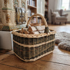 Rectangular wicker basket with handle used as a firewood holder with birch logs beside a tiled stove in a cosy living room