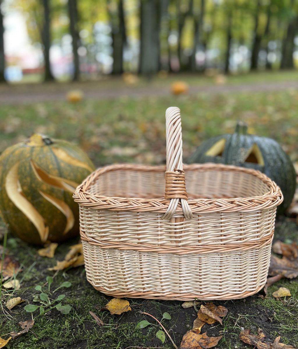 Empty rectangular wicker basket with braided rim on autumn grass with carved pumpkins in the background