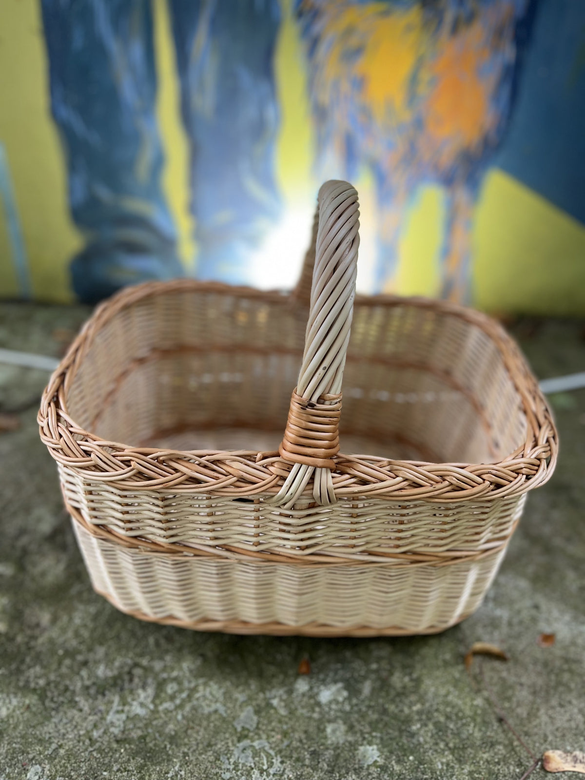 Close view of the rectangular willow basket with a twisted handle and braided rim on a mossy stone ledge