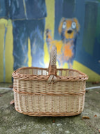 Rectangular willow basket with braided rim and wrapped handle on a concrete ledge in front of a painted street art mural