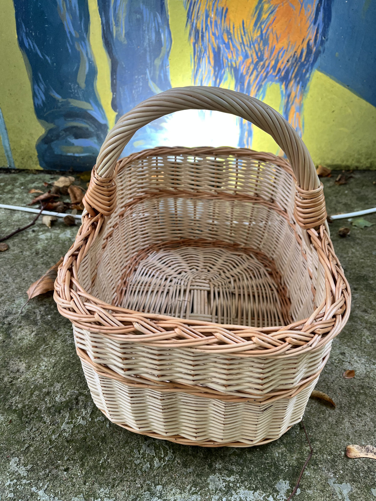 Top view into the rectangular wicker picnic basket showing its woven base, braided rim and arched handle against a painted mural wall