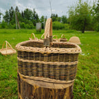 Rectangular willow basket with wrapped handle on a wooden stump in a countryside field with more baskets behind
