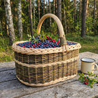 Handwoven willow basket with a tall handle filled with blueberries and lingonberries on a wooden table in a pine forest, next to an enamel mug