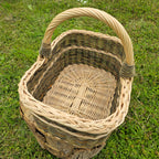 Top view inside the empty rectangular wicker market basket with arched handle, showing the woven flat base and braided rim on a stump