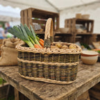 Wicker market basket with handle carrying leeks, carrots and potatoes on a rustic wooden table at a farmers market stall