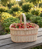 Handwoven picnic basket with handle full of fresh strawberries on a wooden table in a summer garden
