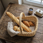 Wicker bread basket with handle holding a baguette, croissants and rolls on a linen cloth on a rustic table with coffee