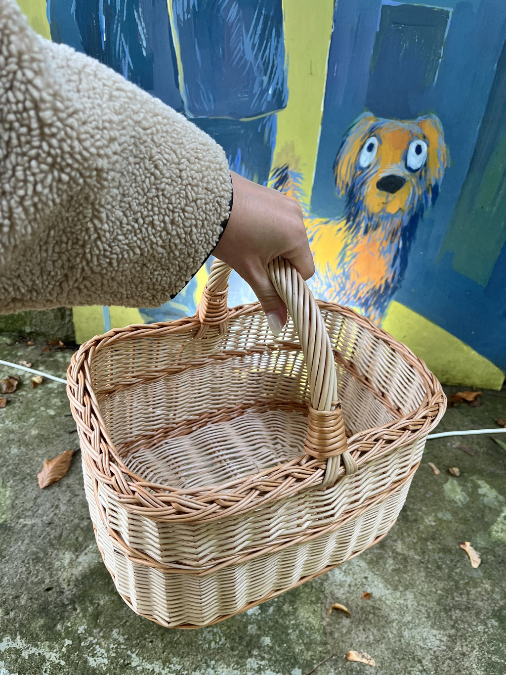Hand carrying an empty willow basket by its wrapped handle in front of a colourful street art mural