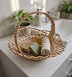 Small open-weave willow basket with an arched handle holding handmade soaps, a bottle of oil and a rolled towel on a bathroom vanity