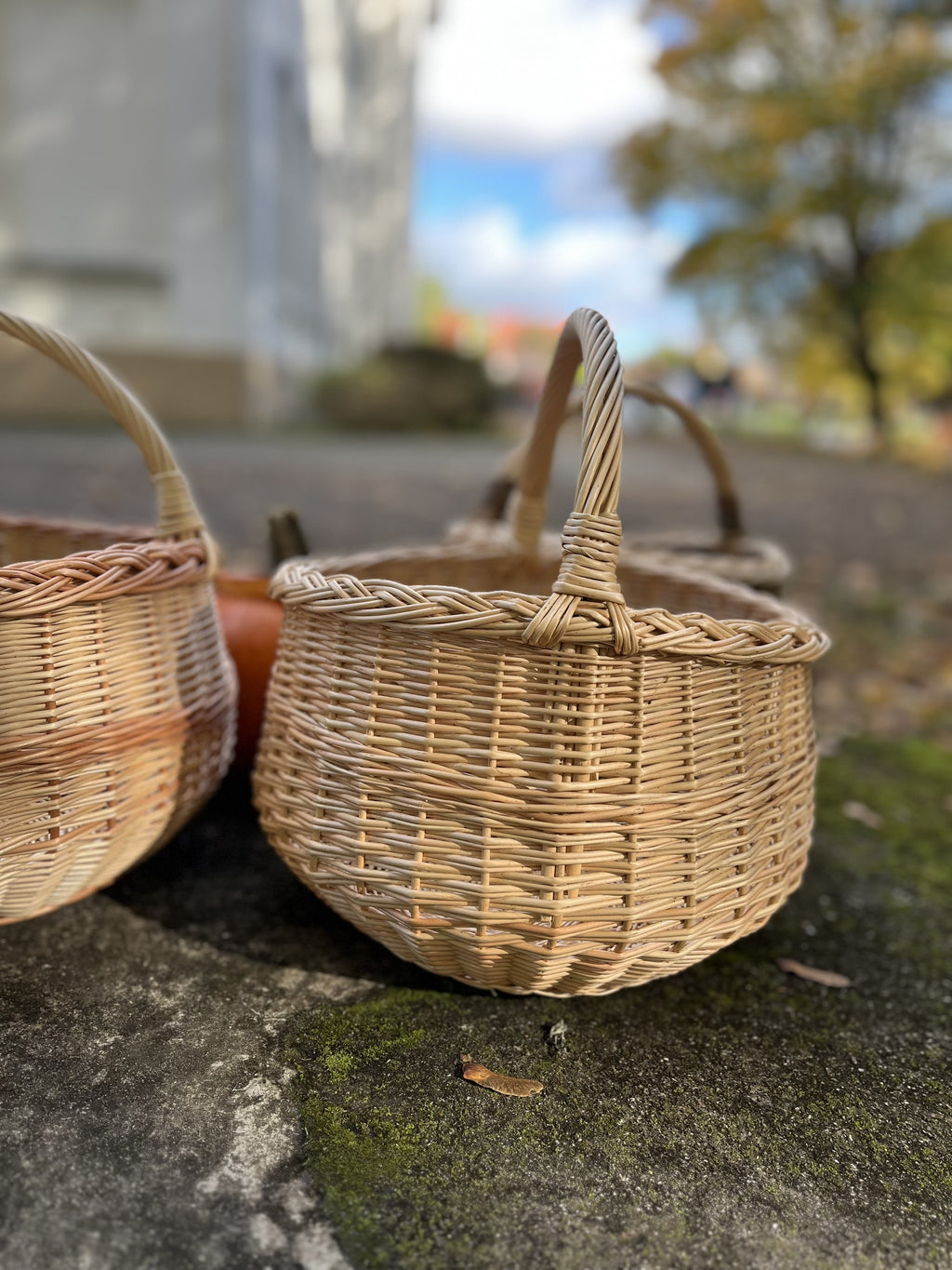 Two round wicker baskets with handles side by side on a mossy stone ledge in an autumn courtyard