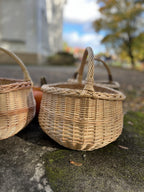 Two round wicker baskets with handles side by side on a mossy stone ledge in an autumn courtyard