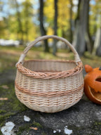 Round handwoven egg gathering basket with arched handle on a mossy rock beside a carved pumpkin
