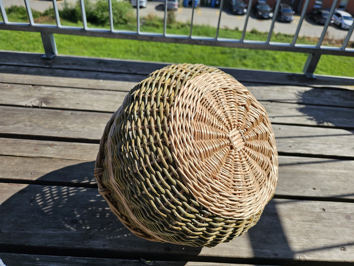 Close-up of the radial woven base of the round handwoven willow basket, turned upside down on a sunny wooden balcony table