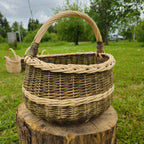 Round wicker basket with braided rim and wrapped handle on a tree stump in a green countryside garden