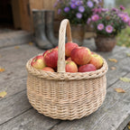 Round wicker basket with handle full of apples on a wooden porch with rubber boots and potted asters behind