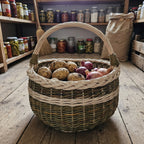 Round wicker basket with handle holding potatoes and onions on the wooden floor of a pantry with jars on shelves
