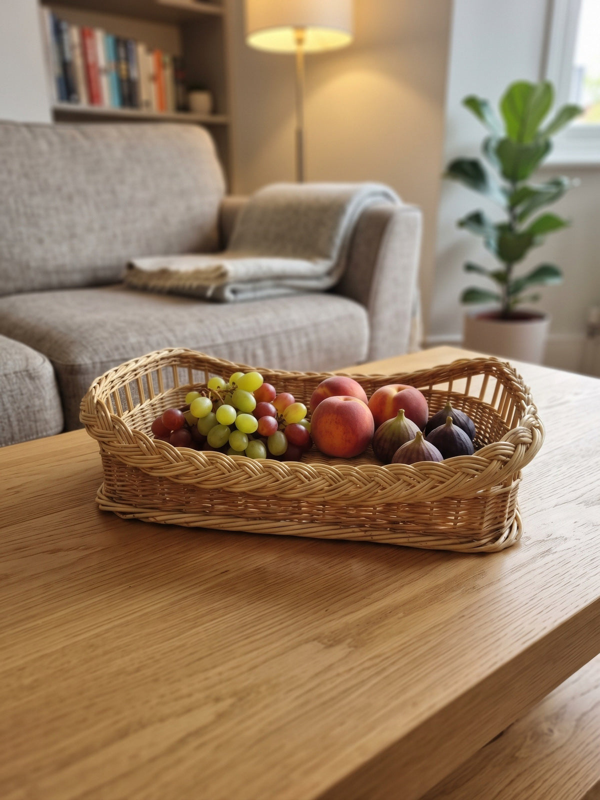 Handwoven wicker tray with raised ends filled with grapes, apples, peaches and figs on an oak coffee table in a cosy living room.