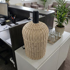 Wicker water cooler cover on a 5 gallon bottle topped with an electric pump, set on a white cabinet in a modern open-plan office