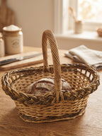 Small oval wicker bread basket with handle holding a round sourdough loaf on a wooden kitchen worktop.