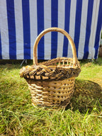 Small oval willow basket with a sturdy arched handle and braided rim photographed on the grass in bright sunlight.
