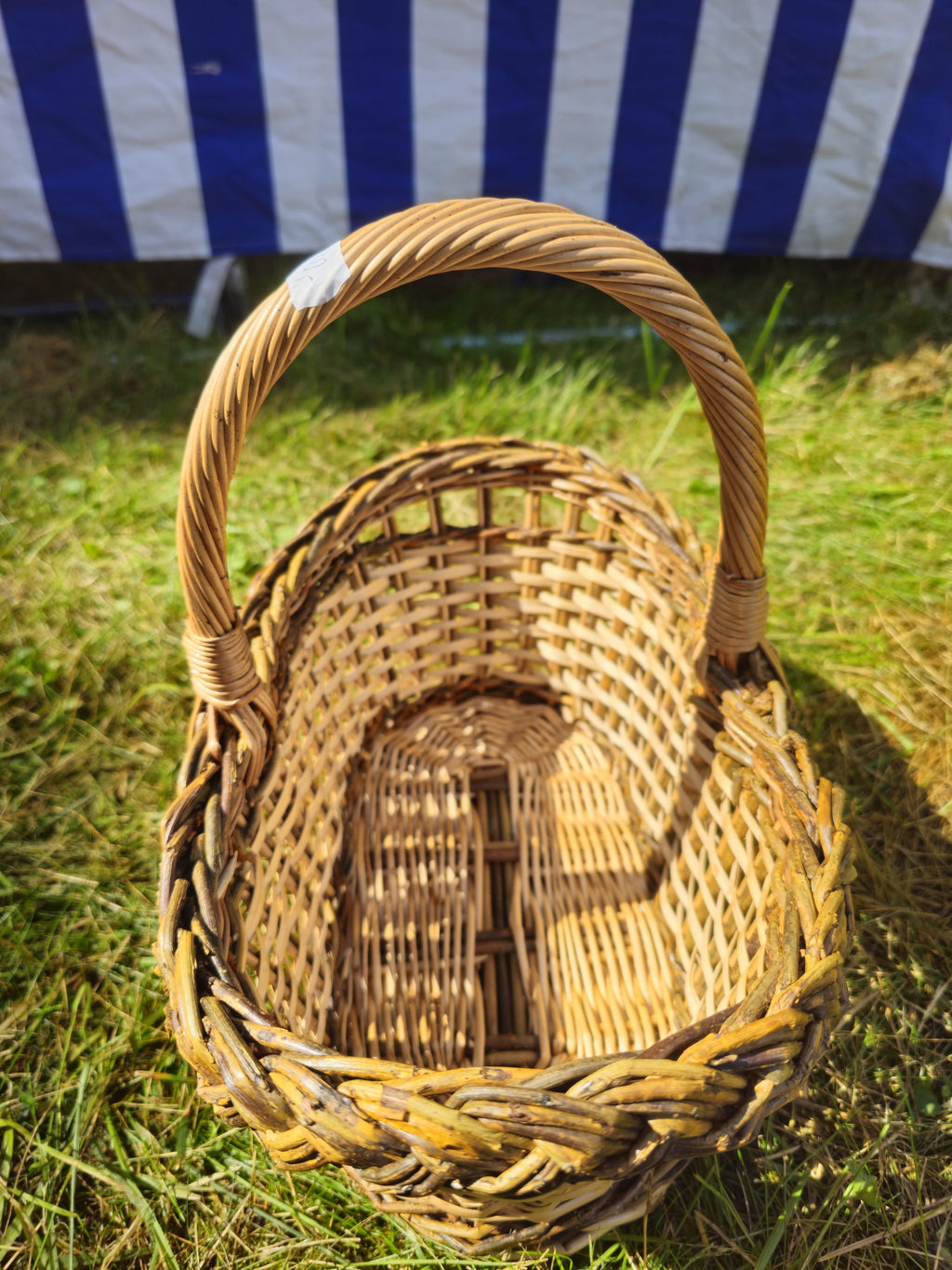 Top view into the small oval wicker bread basket, showing the woven base, braided rim and handle, on green grass.