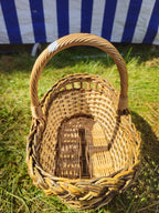 Top view into the small oval wicker bread basket, showing the woven base, braided rim and handle, on green grass.