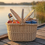 Picknickkorb aus Weide mit Äpfeln, Thermoskanne und Bechern auf einem Holzsteg am See bei Sonnenuntergang