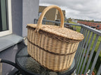 Willow picnic basket with lid seen at an angle on a glass table, showing the double lids, woven bands and arched handle.