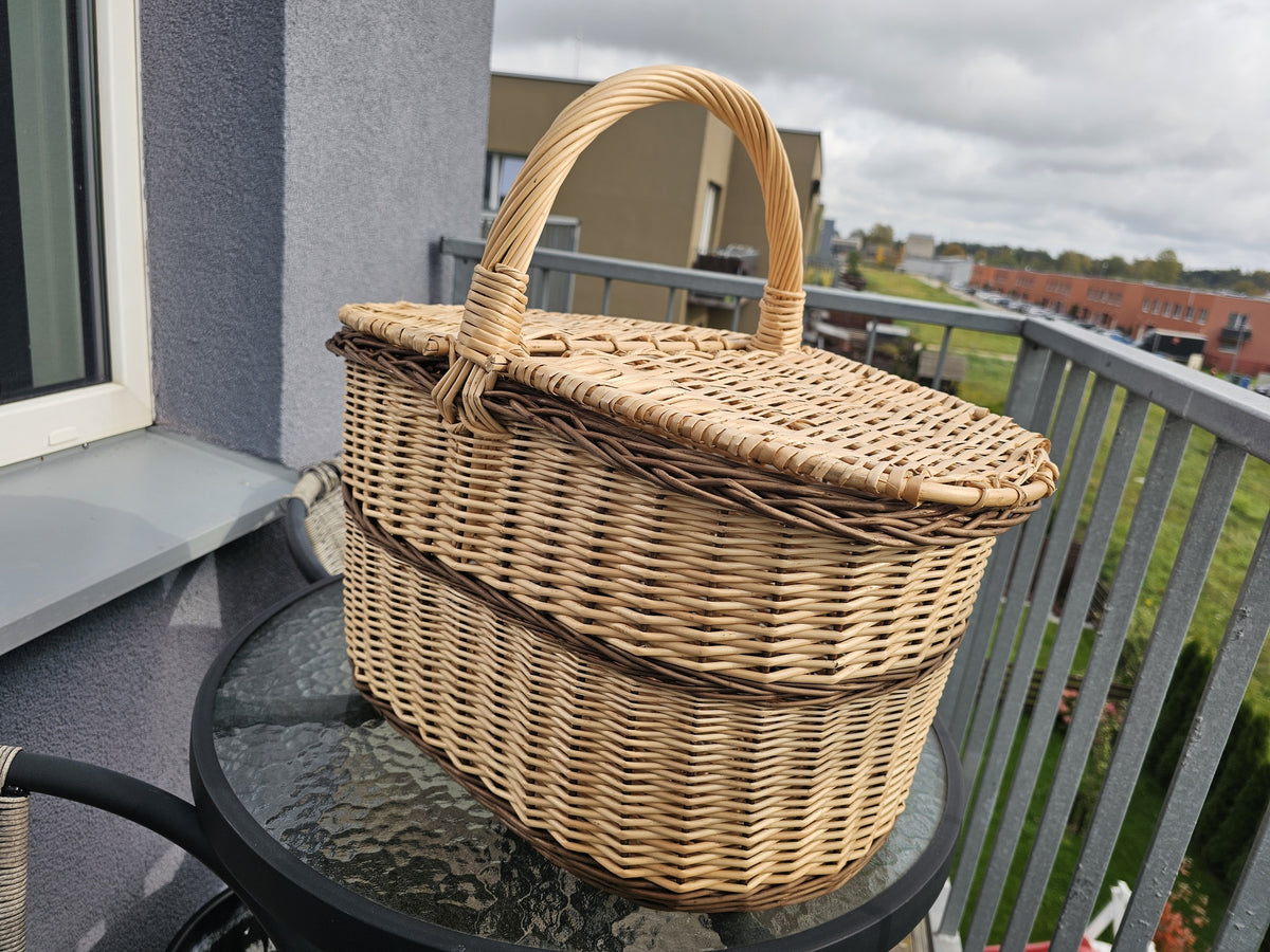 Willow picnic basket with lid seen at an angle on a glass table, showing the double lids, woven bands and arched handle.