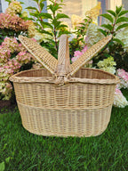 Oval handwoven willow hamper with both lids opened to each side, standing on the lawn in front of hydrangea bushes.