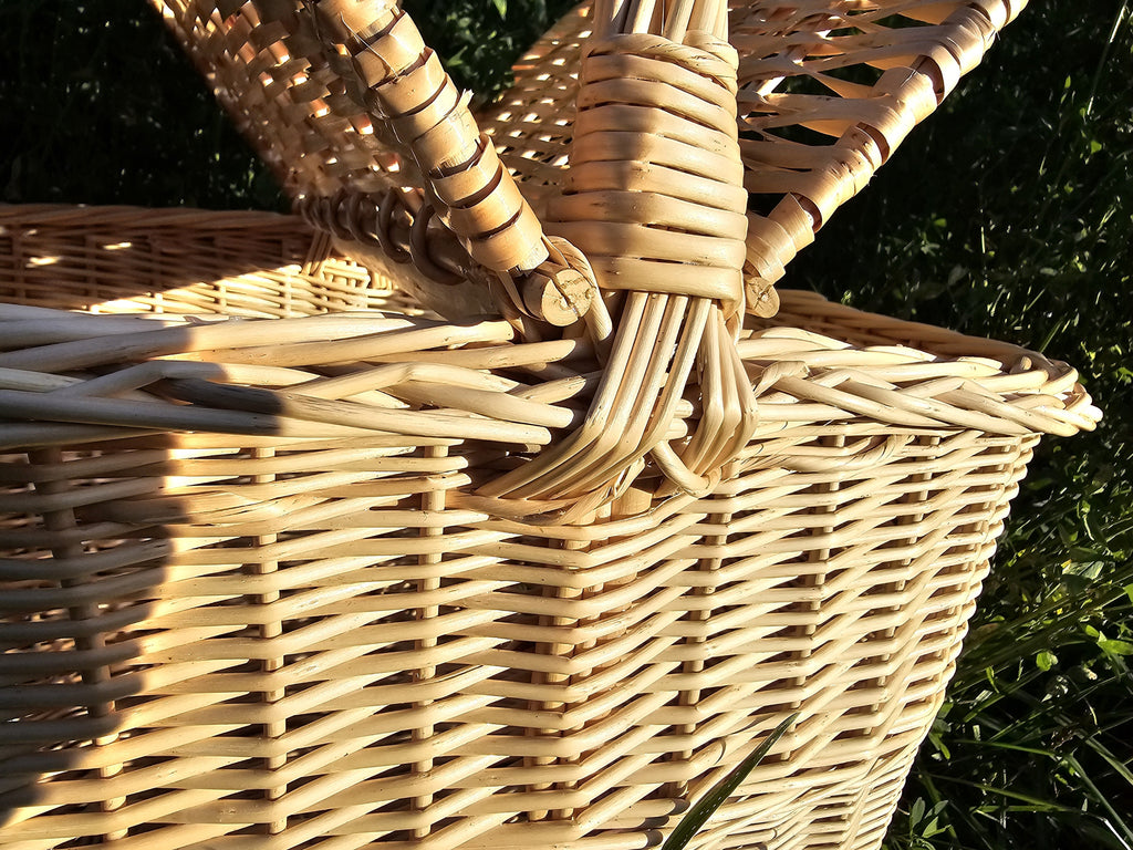 Close-up of the centre handle and hinge loops of the wicker picnic basket with lid, showing the tight hand weave of the oval body