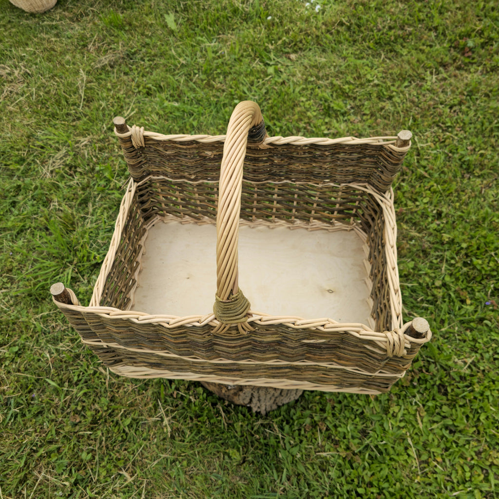 Top view of the handwoven willow firewood basket with corner posts, showing the flat base and the handle across the middle on grass