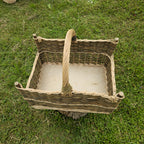 Top view of the handwoven willow firewood basket with corner posts, showing the flat base and the handle across the middle on grass