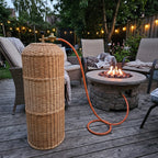 Handwoven willow propane tank cover hiding a gas bottle on a garden deck beside a fire pit, with the valve and orange hose left free at the top