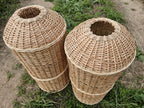 Two wicker gas bottle covers lying on the grass with their dome-shaped tops and central openings, the weave reinforced by horizontal bands