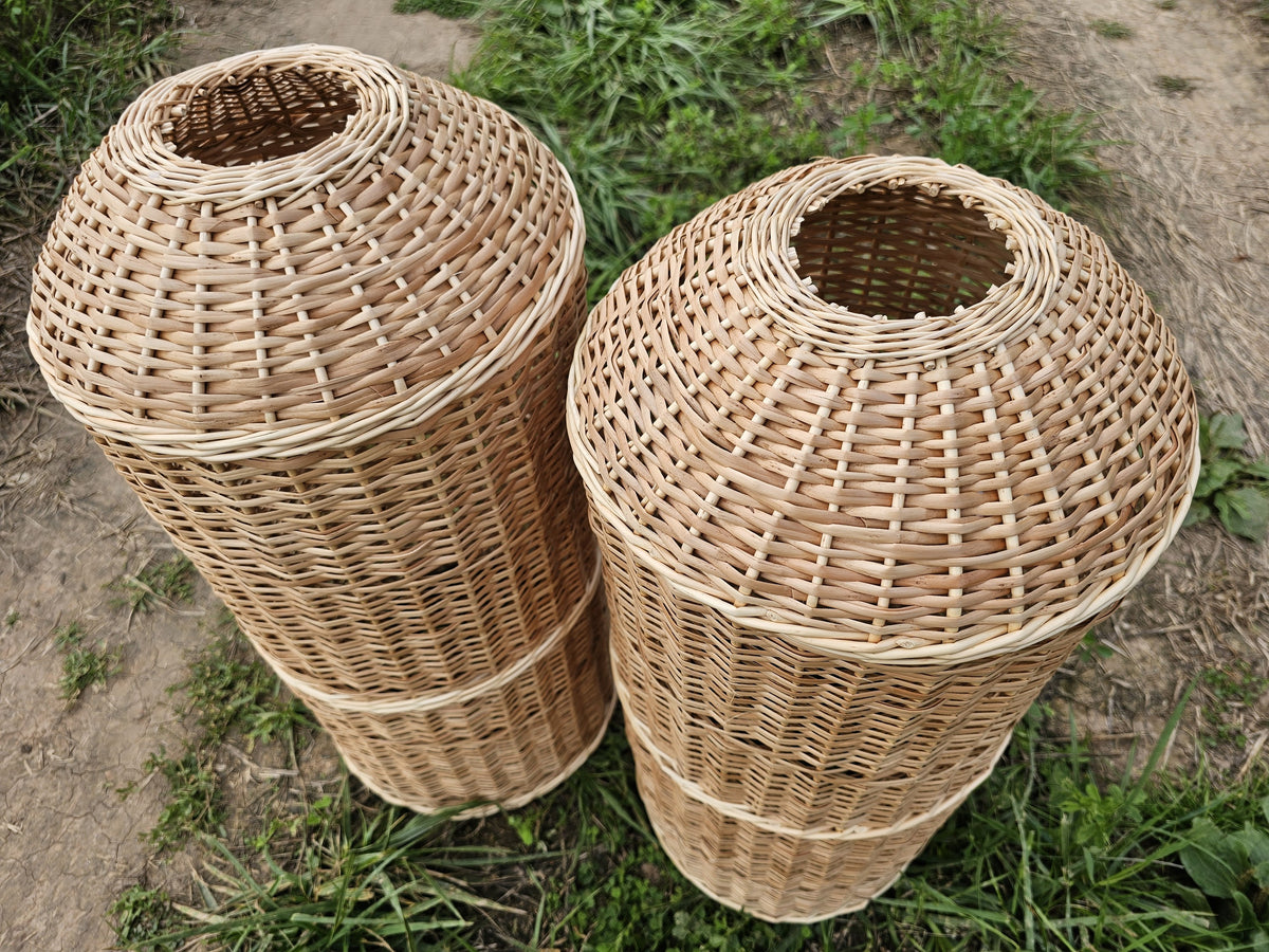 Two wicker gas bottle covers lying on the grass with their dome-shaped tops and central openings, the weave reinforced by horizontal bands