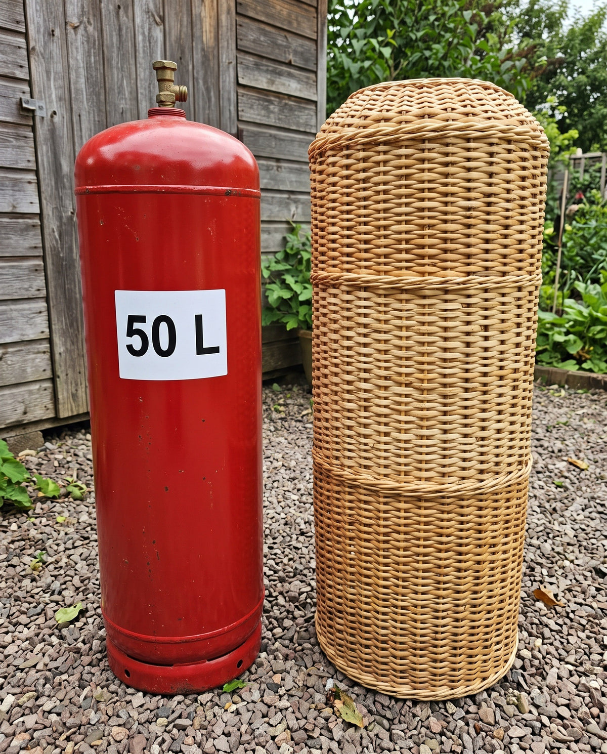 80 cm handwoven willow gas bottle cover standing next to a red 50 L gas cylinder on gravel, showing the matching height of the cover