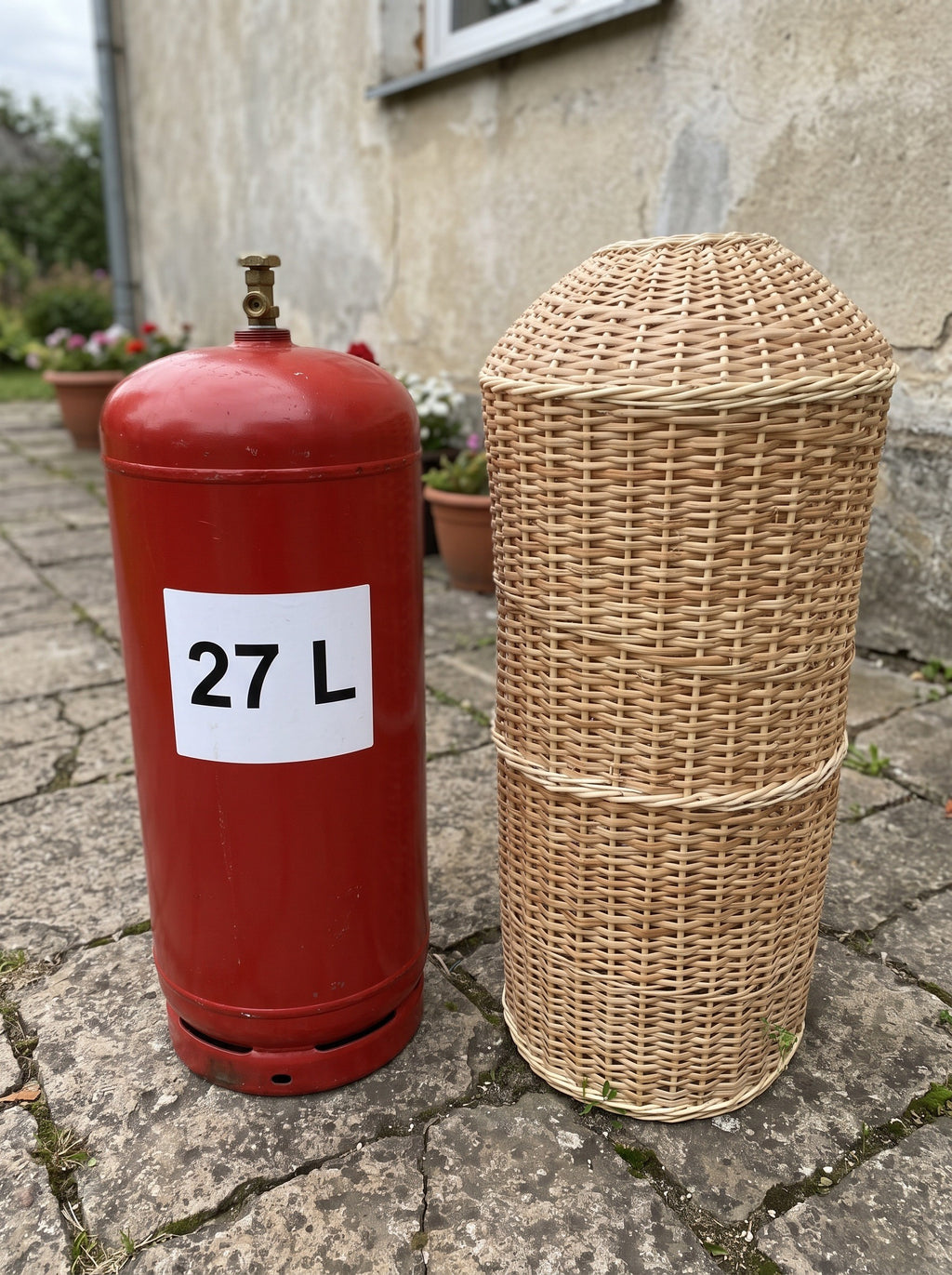60 cm wicker gas bottle cover beside a red 27 L gas cylinder on a stone patio, showing the smaller size of the willow sleeve