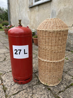 60 cm wicker gas bottle cover beside a red 27 L gas cylinder on a stone patio, showing the smaller size of the willow sleeve